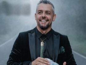 A man in a formal black suit standing on a foggy road while holding a deck of cards