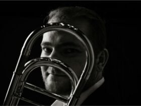 Black-and-white portrait of a trombone player looking through his instrument to the camera.