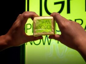 Person holding a camera obscura infront of a neon green sign, turning the sign upside down