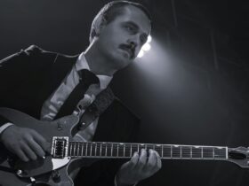 A black and white image of a man in a suit playing guitar