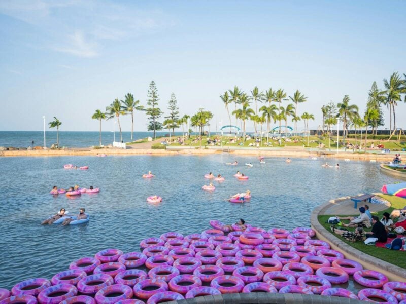People floating on pink inflatable rings in a large seaside lagoon at The Strand in Townsville.