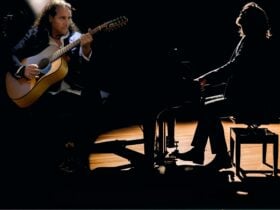 Two musicians performing on stage under low lighting: one playing an acoustic guitar and the other s