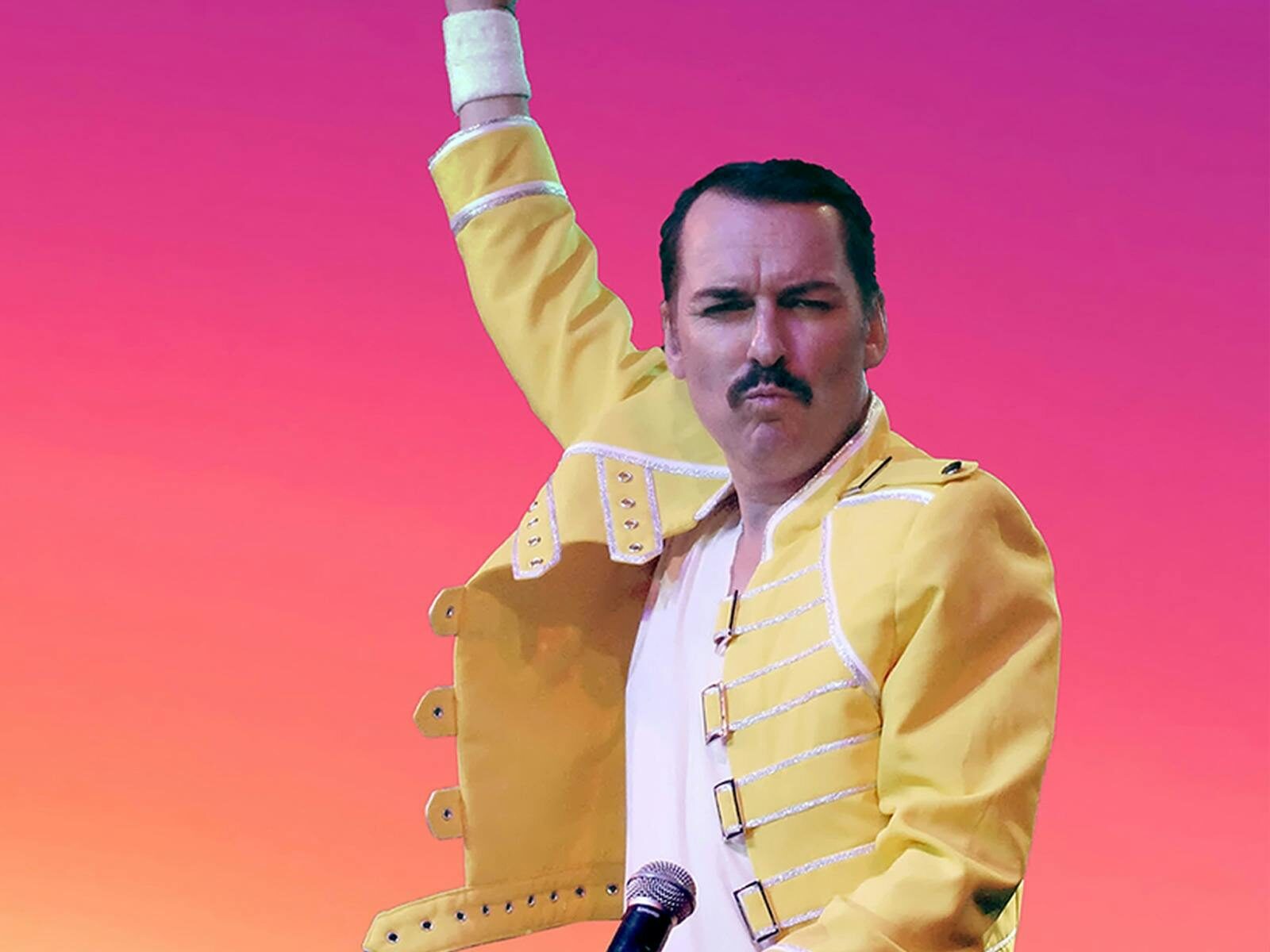A man with a moustache is performing as Freddy Mercury is dressed in a yellow blazer.