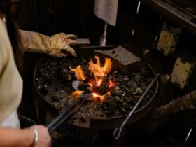 A blacksmith heats something over the coals in a forge.