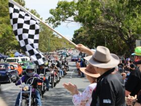 Motorcycles and cars in a street parade watched by crowds during Rockynats.