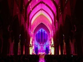 Musicians perform in a large cathedral dramatically lit in coloured light.