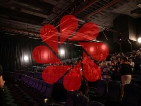Image of a movie theater filling up with a red iris from a camera lens played in front of