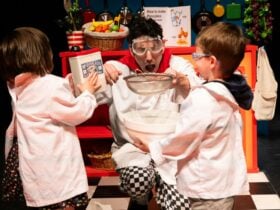 A person in goggles, holding a sieve over a mixing bowl, looks surprised in a playful kitchen scene
