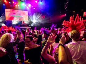A crowd of ladies dance in front of the stage and bright stage lights, some wear feathered headbands