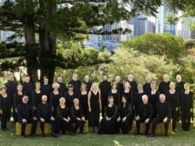 Photo of choir in uniforms standing in rows under a large pine tree.