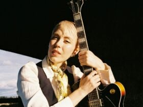 Blonde young women with a pixie cut, leaning her head on a guitar