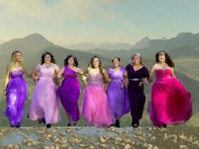 7 women in pink dresses walking through a mountainous landscape.