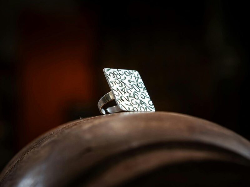 Close-up of handcrafted metal ring with square face and numbers etched on to make pattern.