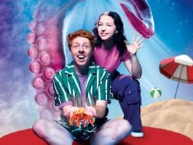 A man in a green and white striped shirt holding a crag with a woman standing behind the man waving