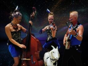Three musicians in matching outfits are holding wooden instruments around a life sized goat model