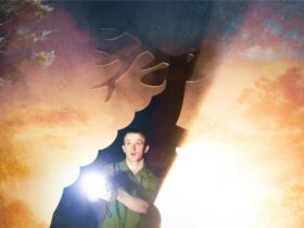 A young man is shining a torch in the bush, revealing the outline of a deer with big antlers