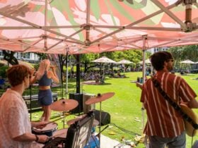Band playing under a marque in a park to audience on picnic rugs