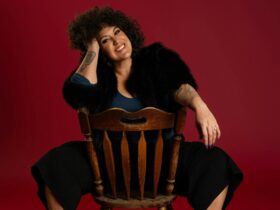 Casey Donovan sitting backward on a chair, leaning on chair top, her legs on either side of chair