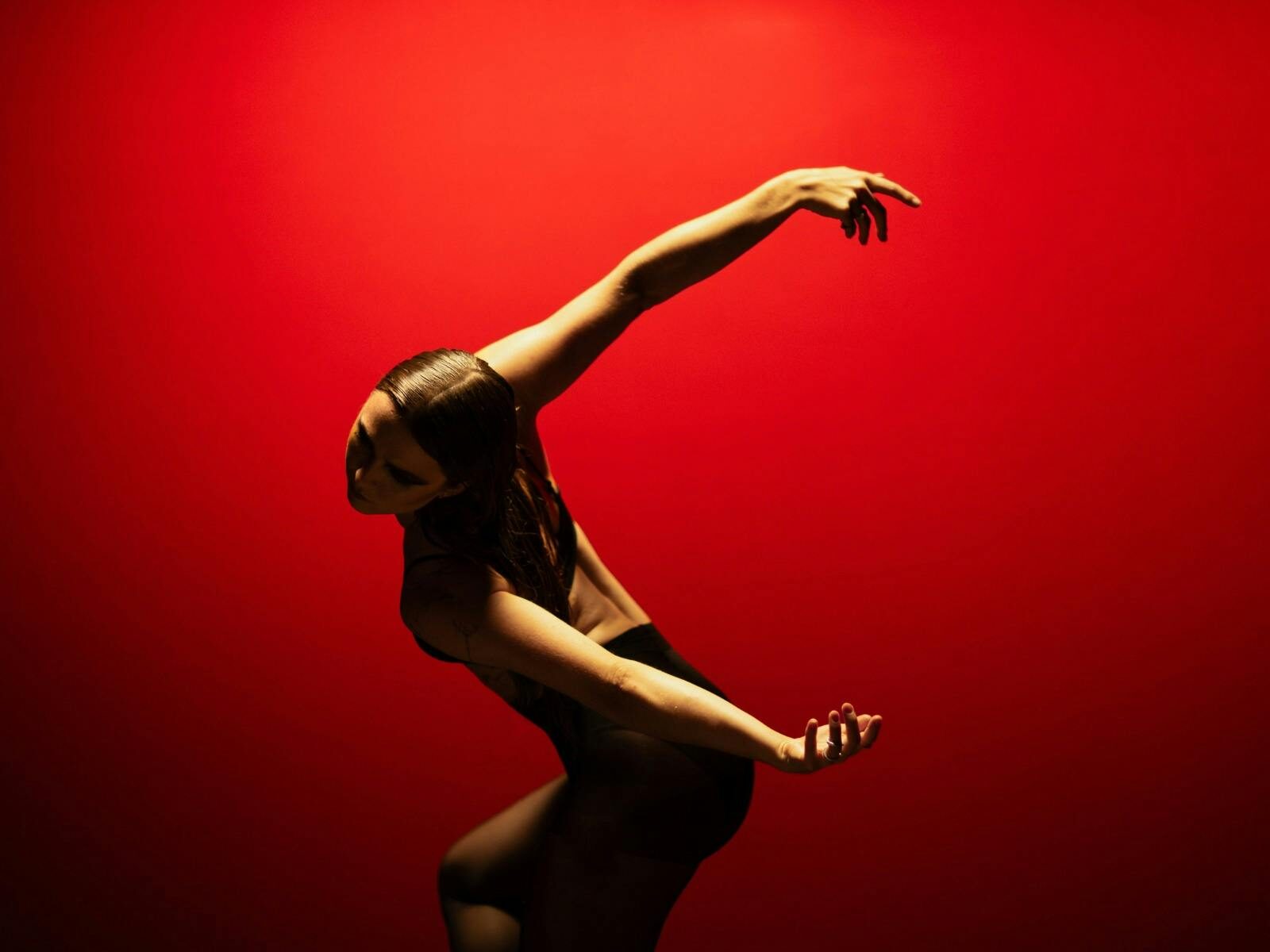 Dancer posed with arms outstretched behind them in front of a bright red backdrop.
