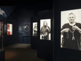A dark gallery space with illuminated portraits of women holding sentimental objects