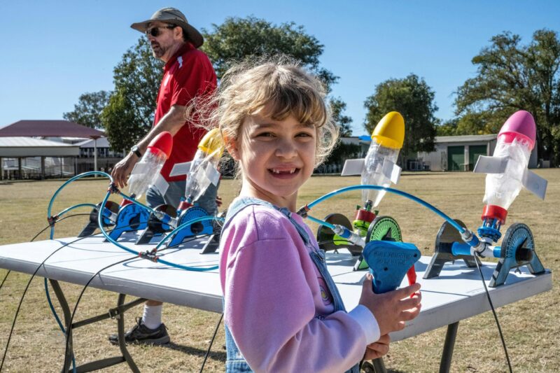 A small girl in a pink shirt in front of colourful bottle rockets