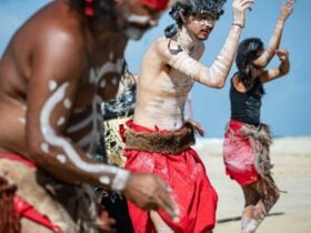 Three Gubbi Gubbi dancers perform on the beach