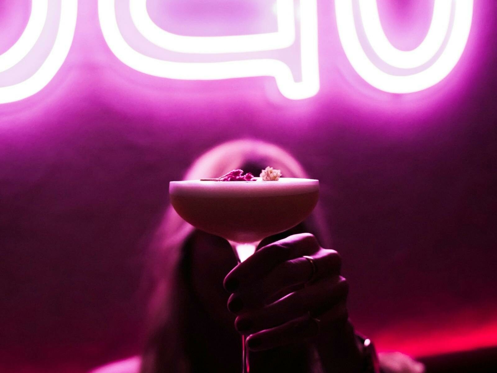 In front of the restaurant sign, a woman holds the signature cocktail.