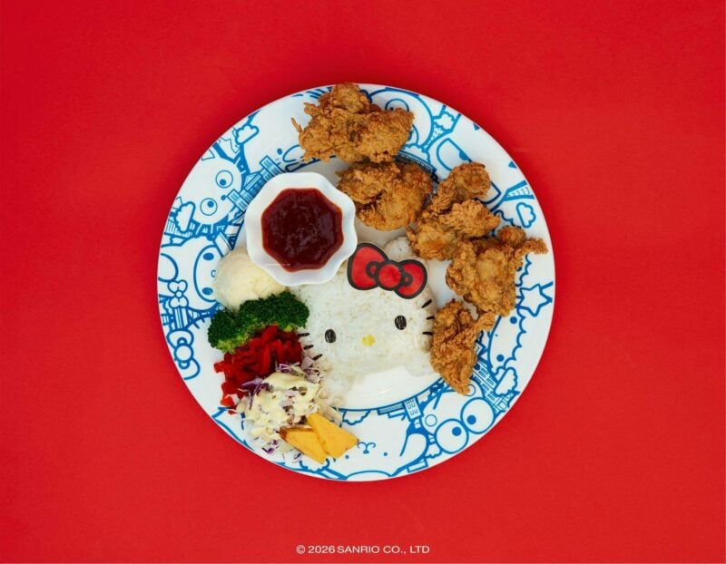 A Hello Kitty-shaped rice ball served with fried chicken, vegetables, and sauce on a plate.