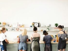 five people standing at a kitchen bench, cooking.