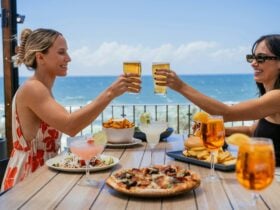 Two women toasting with beer over a table of food dishes