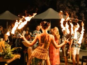 Image of a female fire performer holding a fire staff in each hand with guests watching
