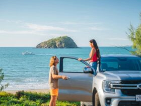 Two tourists pause to look at a boat and a distant mountain rising from the sea