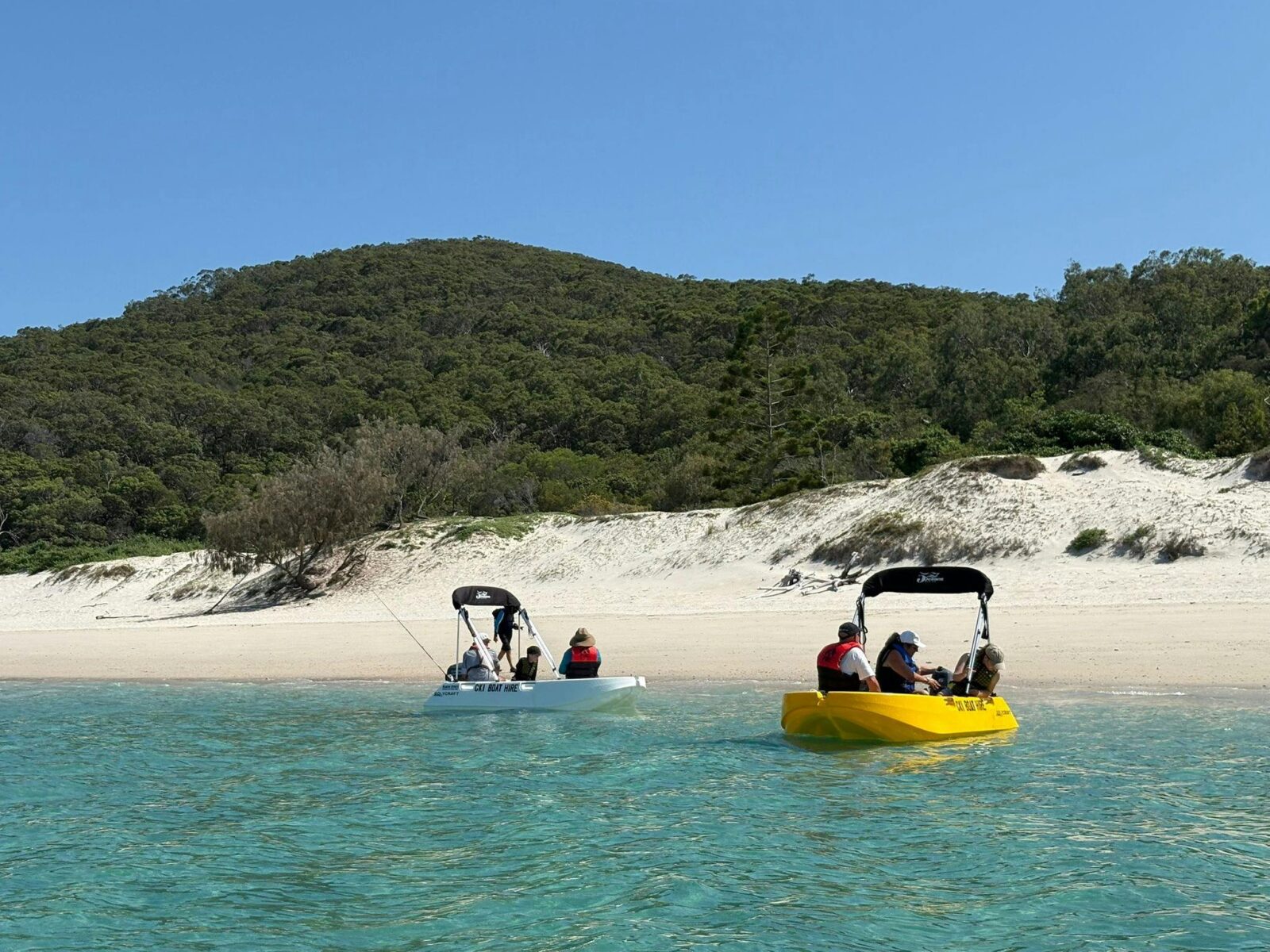 Two Polycraft hire boats near a sandy beach with guests onboard at Great Keppel Island.