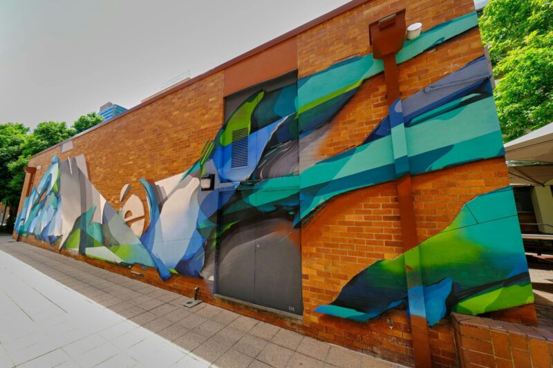 Blue and green street art piece on red brick wall
