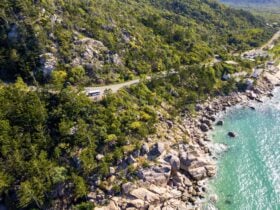 Drone shot of tour bus travelling a mountainside road, overlooking oceans