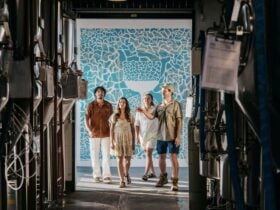 group of 4 people stanidng in door way, foreground is stainless steel fermentation tanks