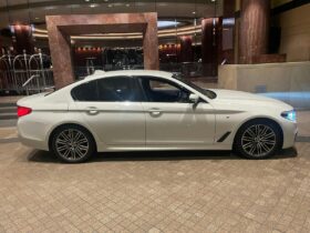 he First Chauffeurs white BMW 5 Series sedan at a luxury hotel entrance