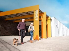 A couple exits Beau's Pet Hotel, walking their dog on a leash.