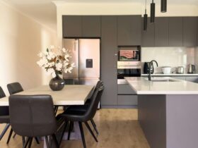 Modern kitchen and dining area with dark cabinetry, dining table and decorative flowers.