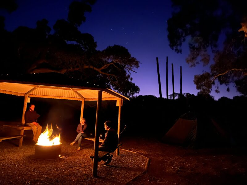 Please sitting around a campfire within campfire circle under shelter and night sky