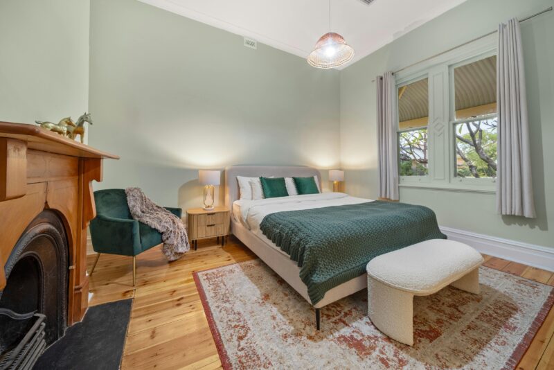 Elegant bedroom with soft greens, plush bed, lamps, velvet chair, vintage fireplace, bench.