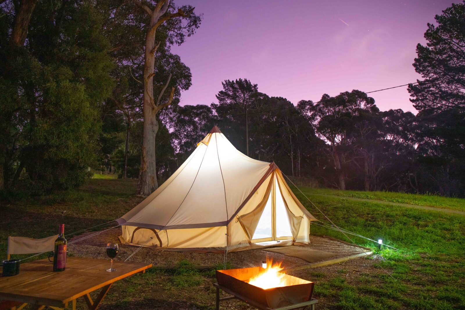 Glamping bell tent at dusk with campfire in front of the tent and trees in background at Woodhouse