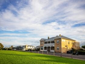 Long distance exterior shot of YHA Port Elliot framed by green grass and blue sky