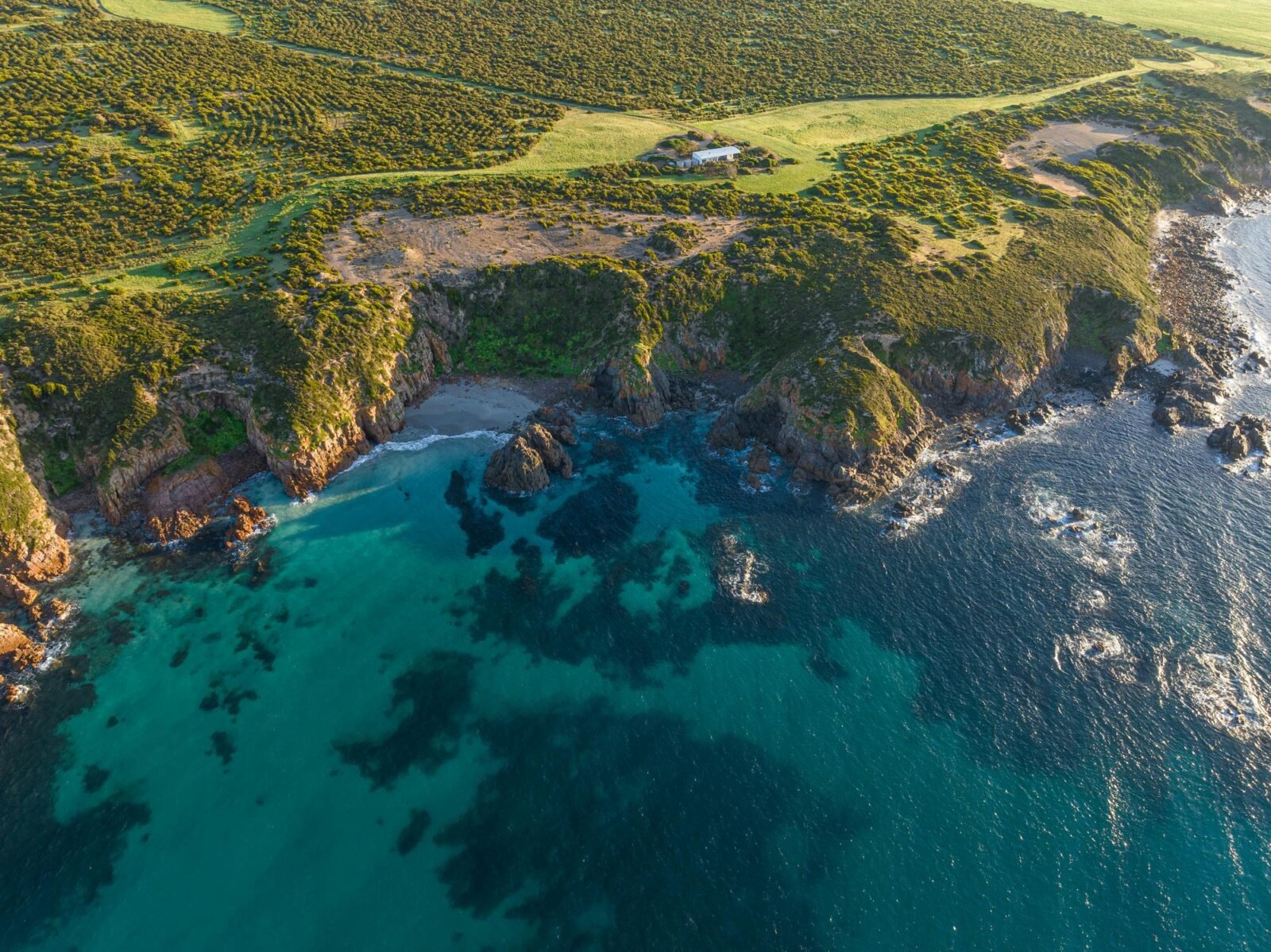 Aerial view of Yondah Beach House showing the house perched on cliffs above a beach and blue ocean