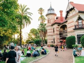 Families sitting on lawns enjoying picnics with a large historic house in the background.