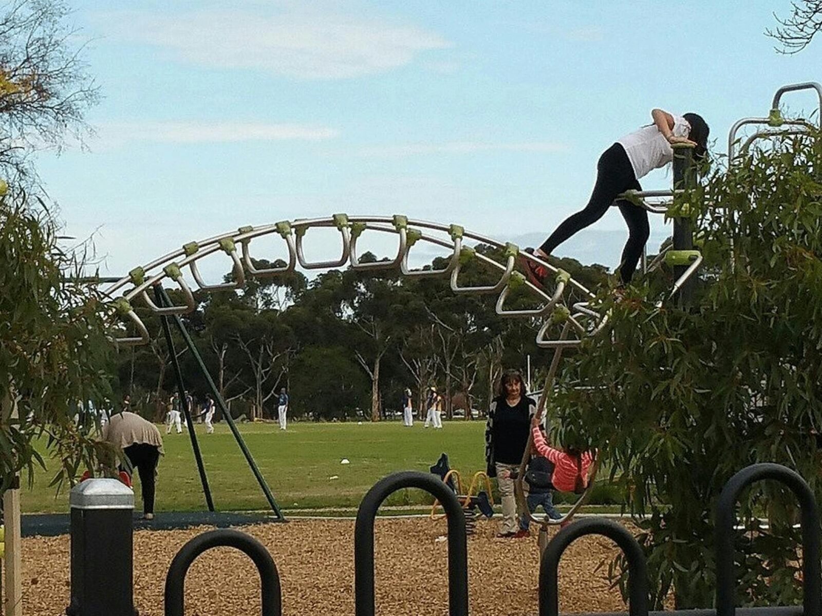 A girl climbing on play equipment at a playground while a local cricket game plays in the background
