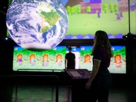 A silhouetted person looks at a globe of the world; in the background, a person plays a video games