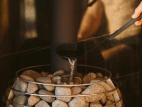 A male figure using the sauna ladle to pour water on the hot sauna rocks creating sauna steam