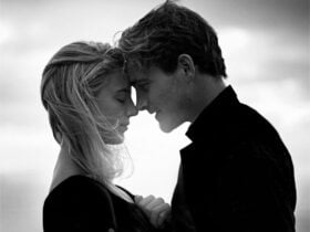 Black and white closeup of a couple facing each other with their foreheads and noses touching. One h