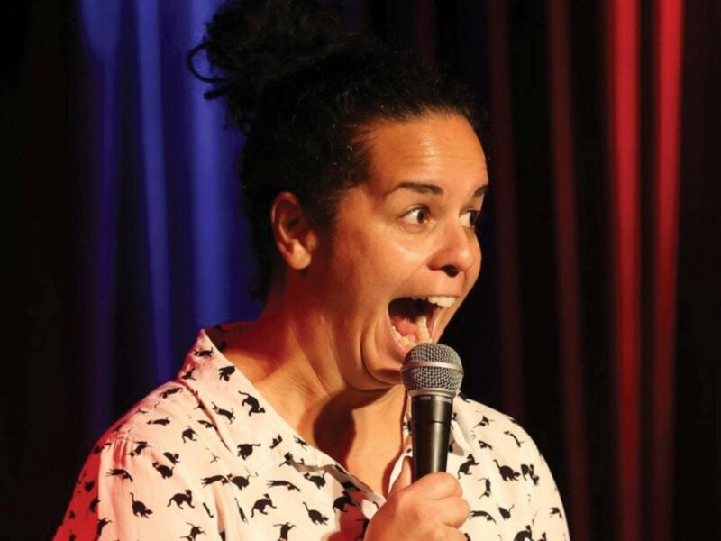 Women is holding a mic, looking at the audience with a big expression on her face